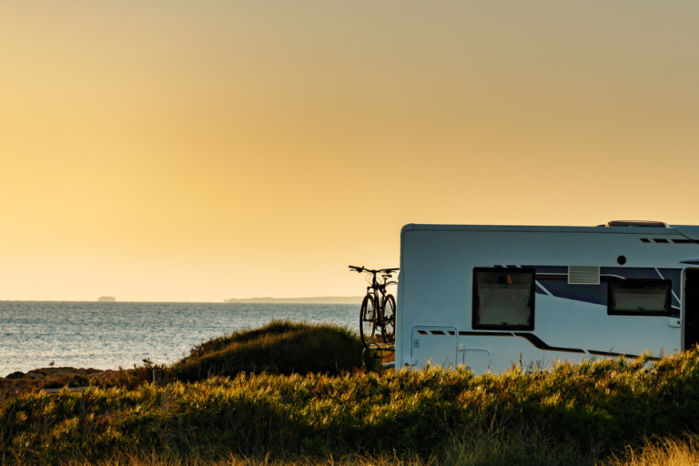 Travel Trailer parked next to the lake with a glowing sunset illuminating the sky behind it