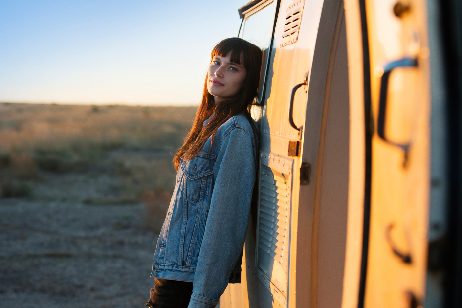 A woman stands leaned against her RV looking directly at the camera