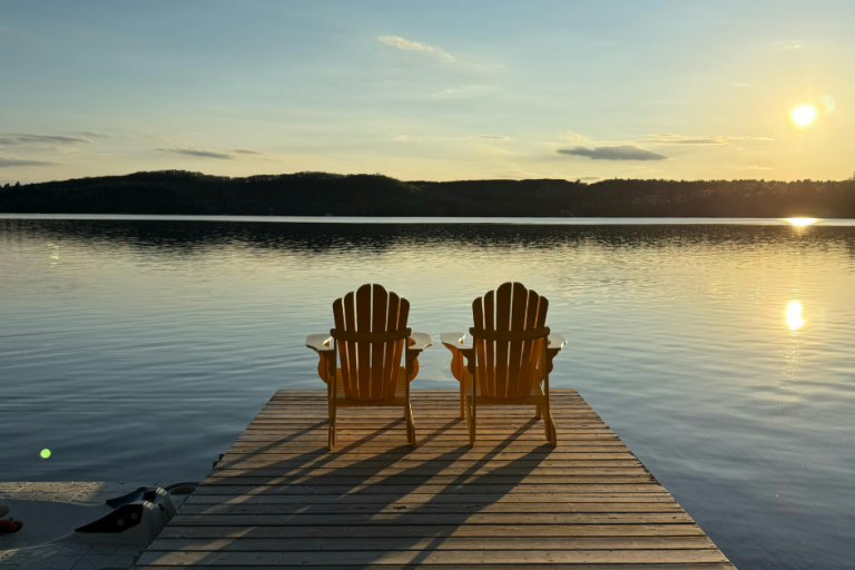 A pair of Adirondack chairs sit at the end of a doc overlooking Lake Superior in Ontario at sunset.