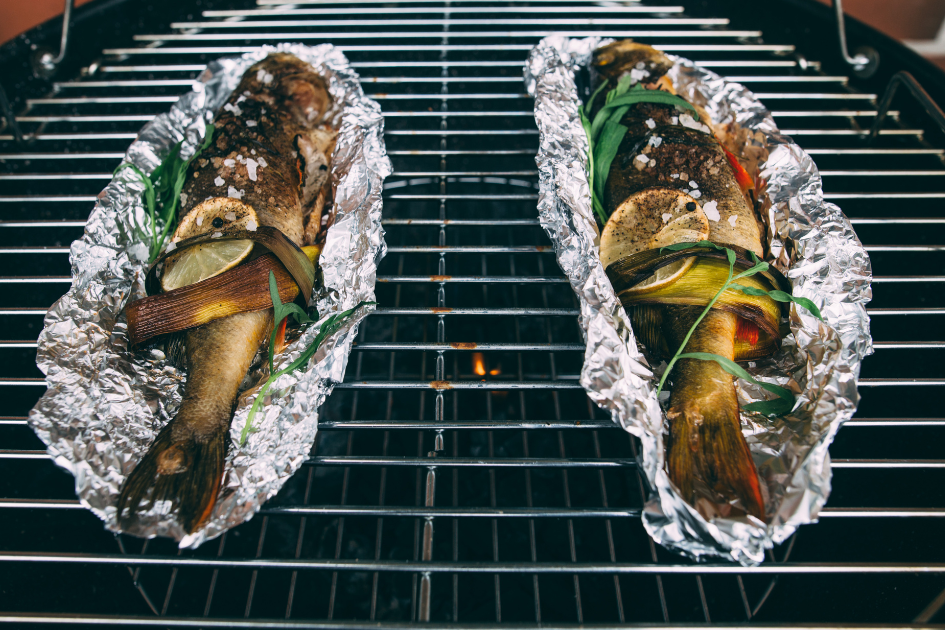 Grilled fish over a camping BBQ in foil with roasted vegetables. 
