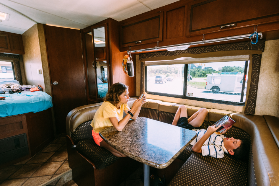 A brother and sister relax at the kitchen table inside their family RV