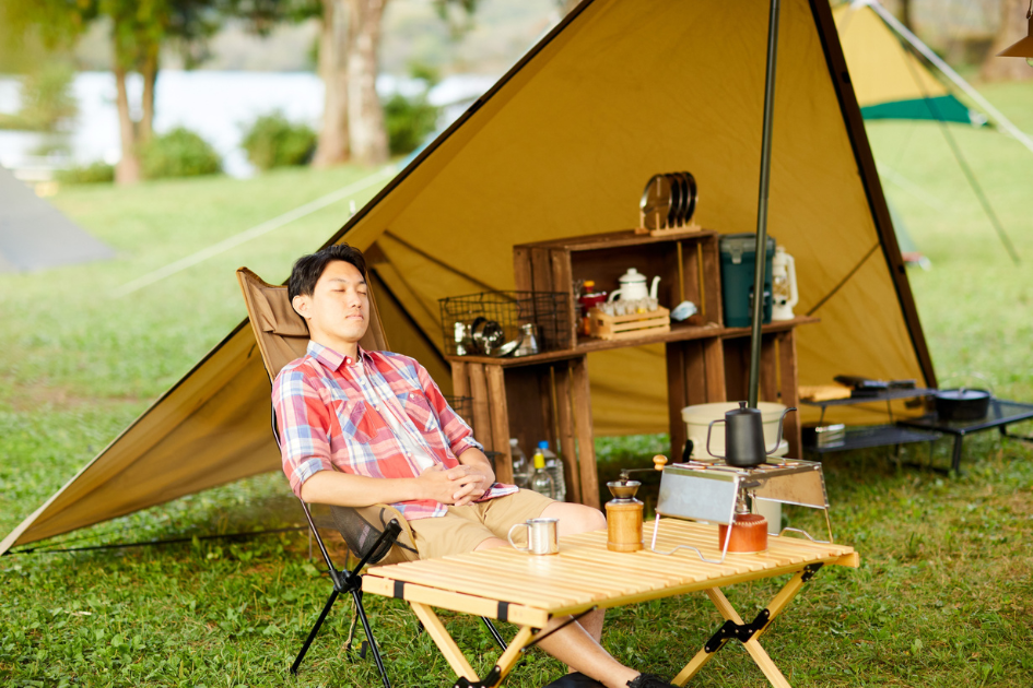 A man naps in a recliner chair underneath a tarp put up for shade on a sunny day. 