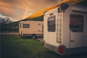 Two travel trailers parked side by side in a grassy spot with a sunset and rainbow in the background