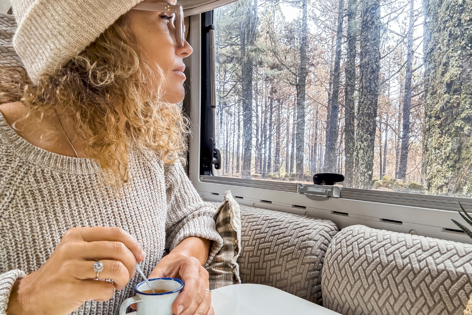 Woman sits at her RV window looking out at the fall landscape