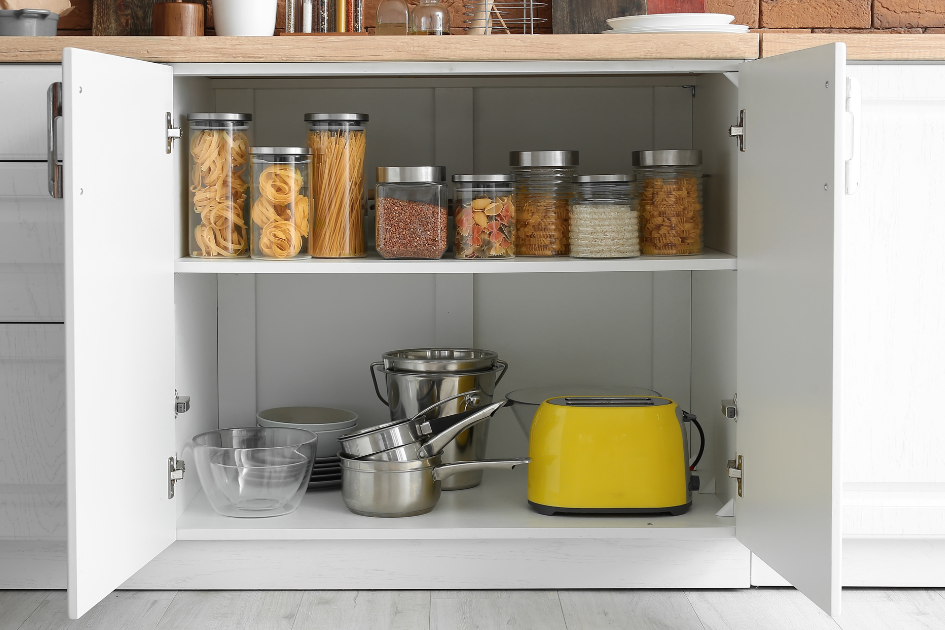 RV kitchen cupboard organized with clear storage containers, and camping cookware