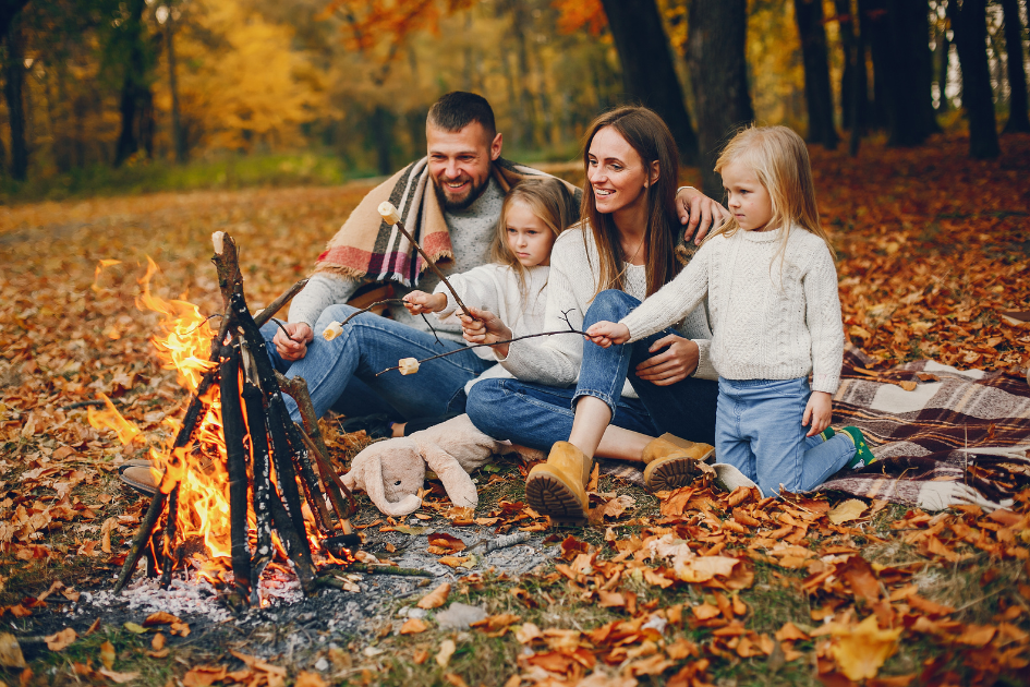 Family sits on a blanket in a beautiful fall camp spot roasting marshmallows
