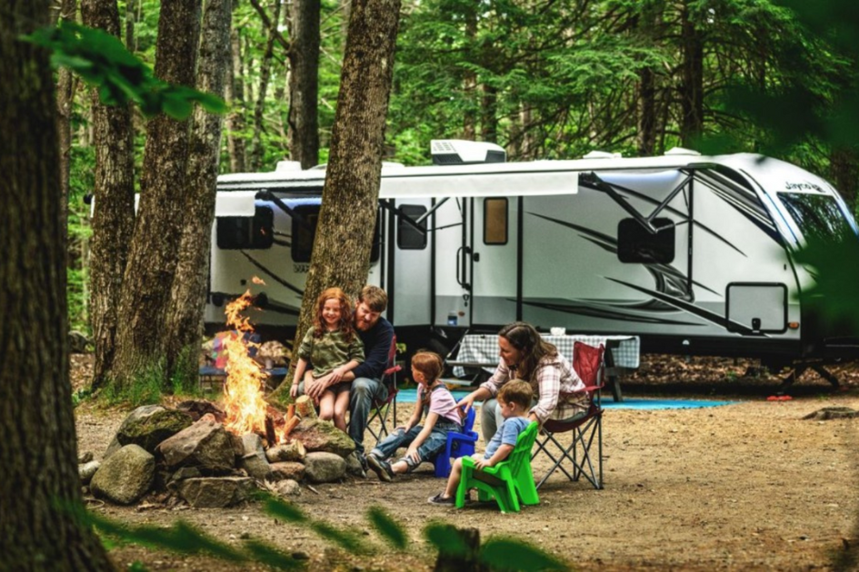 A family gathered around a fire, enjoying an RV vacation in the woods, one of the three main outdoor travel trends we're seeing this year.