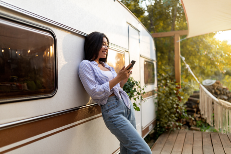 Woman stands outside her parked travel trailer checking her phone
