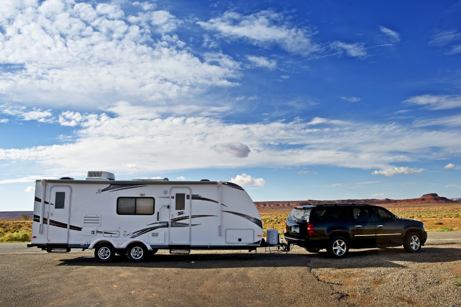 An SUV with travel trailer in tow, parked in an open stretch of land