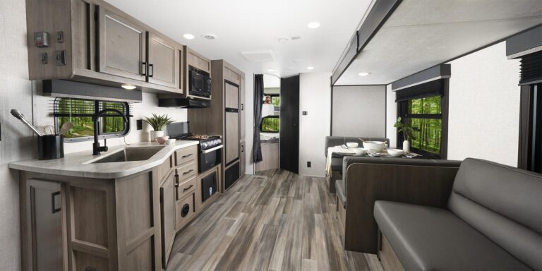 A panoramic shot of an RV's interior living area, including a spacious and beautiful kitchen, a sofa, and a dinette.