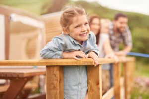 Family leans over a fence in front of their parked RV, all smiles