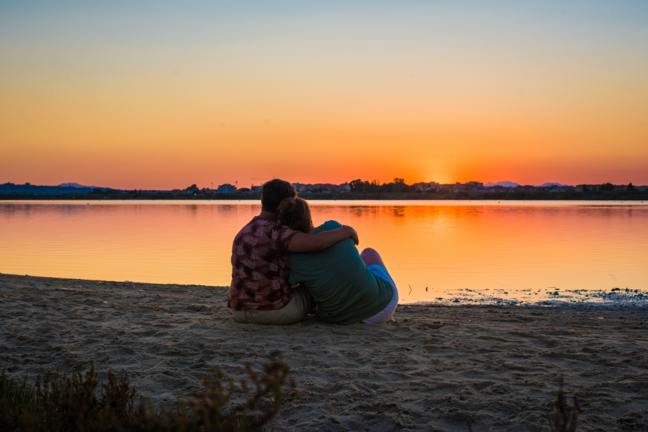 A couple sits on a beach watching the sun go down. 