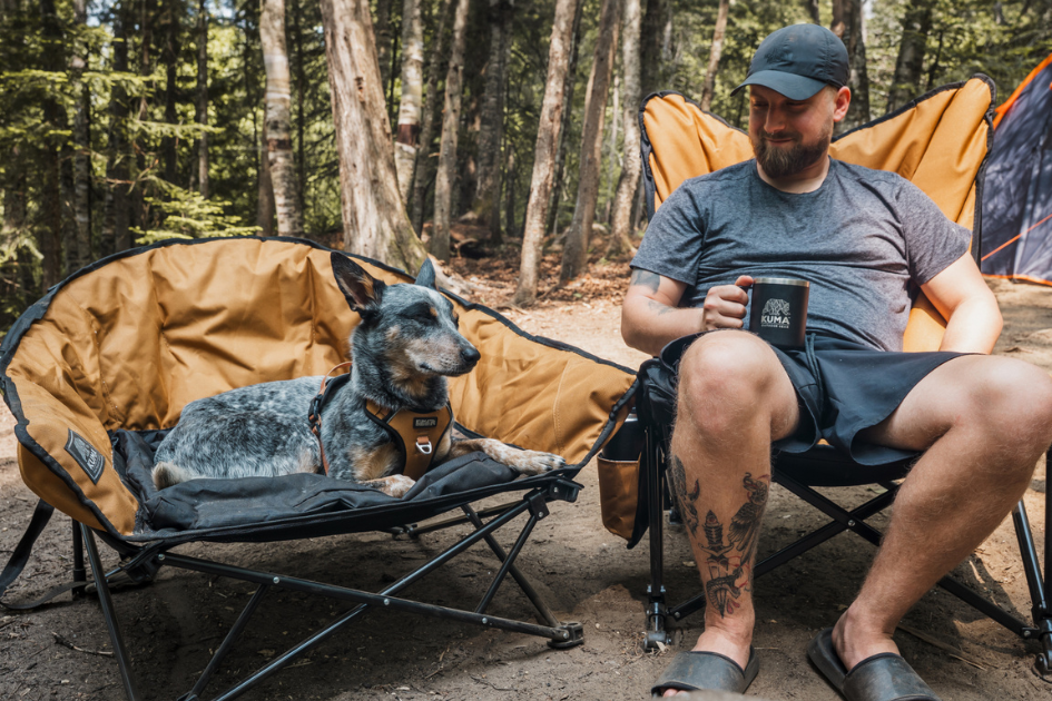 A mand and his dog sit in their own Kuma camping chairs